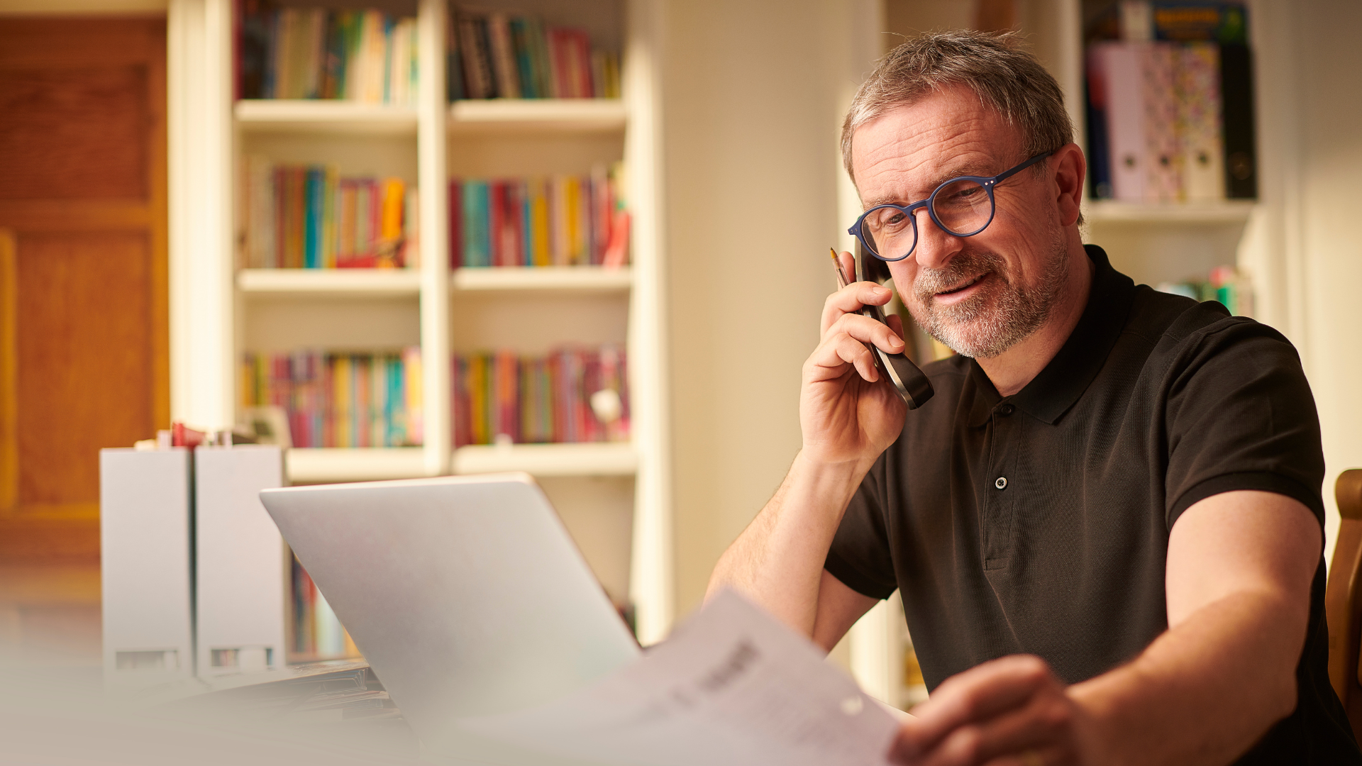 Person on phone at desk disucssing bookkeeping, A small business owner reviewing financial documents with a calculator and laptop, emphasising the significance of accurate bookkeeping.